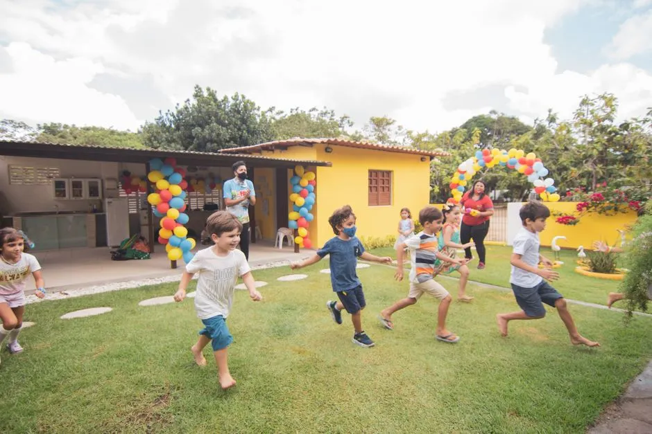 Kids running across a lawn in front of a house decorated with balloons for a birthday party